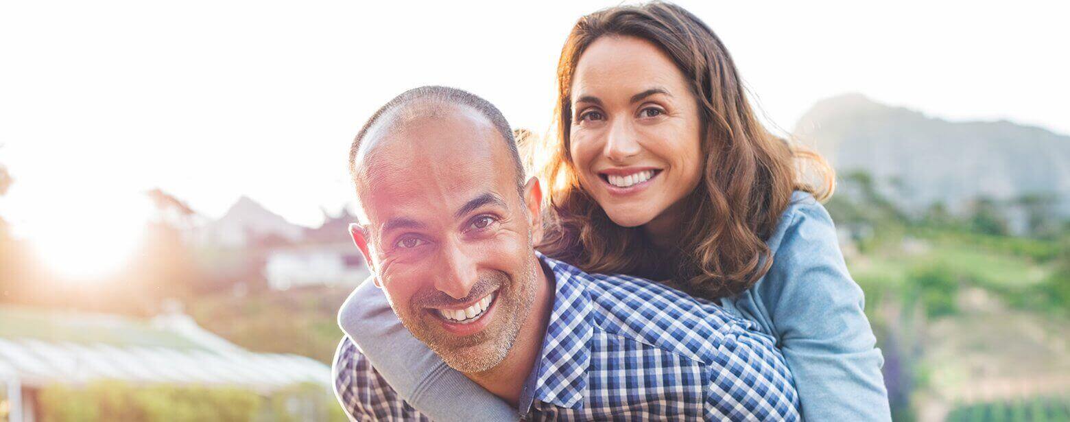 A man smiling as he gives his wife a piggyback ride at sunset