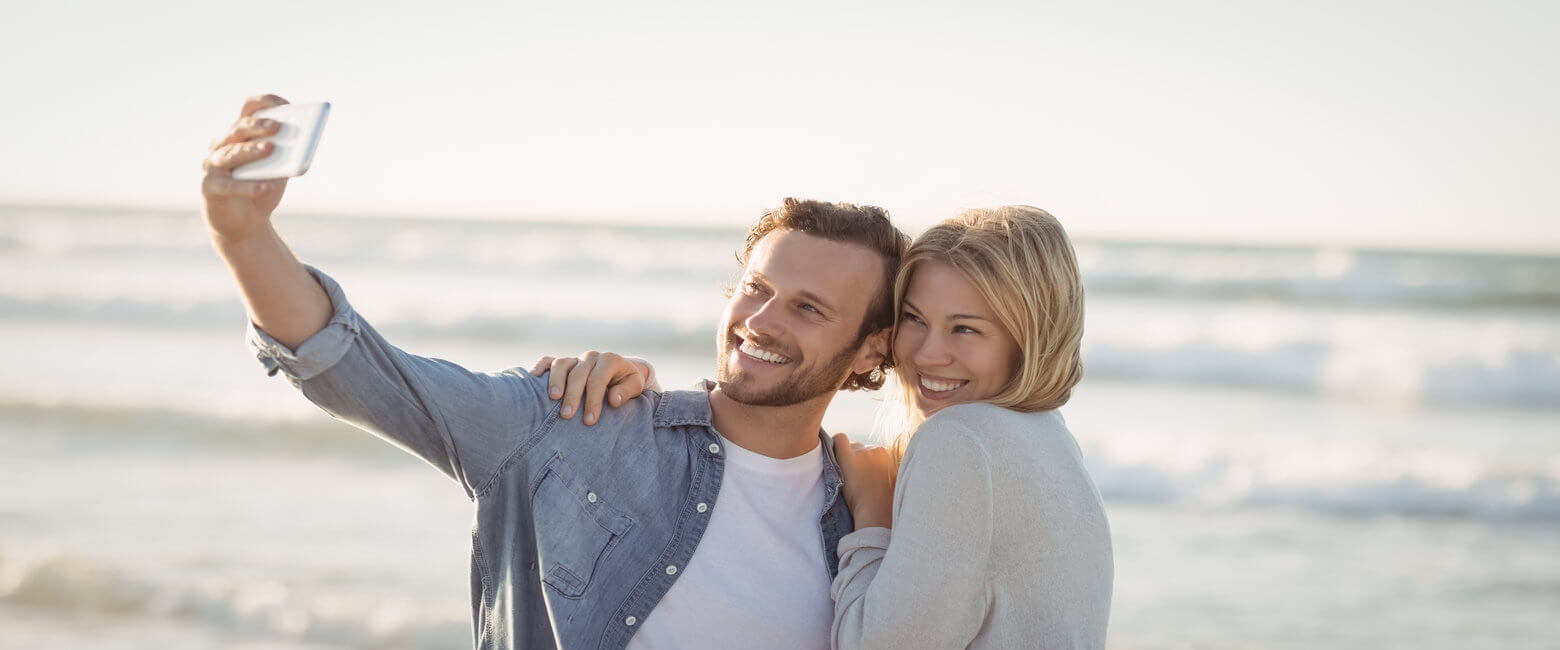 Happy couple taking selfie at beach during sunny day