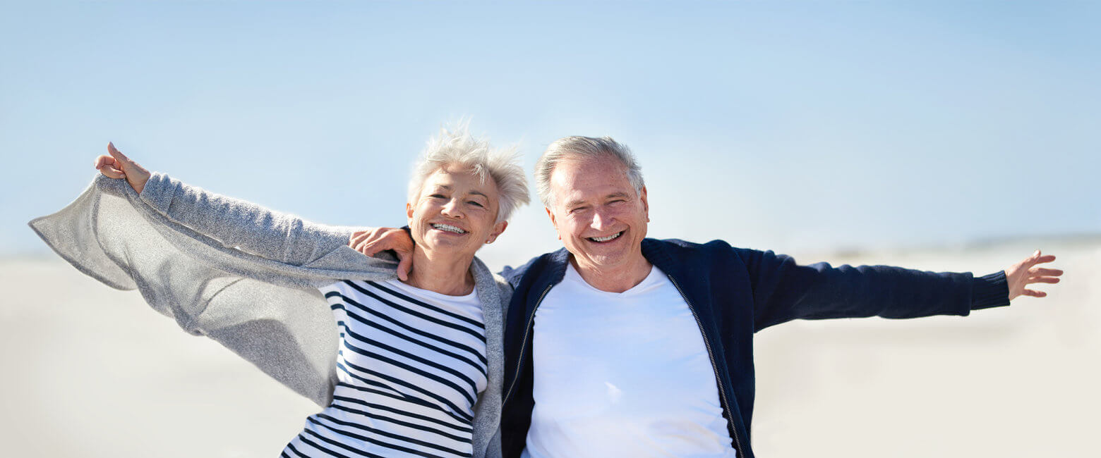 Portrait of a happy senior couple having fun with their arms outstretched at the beach