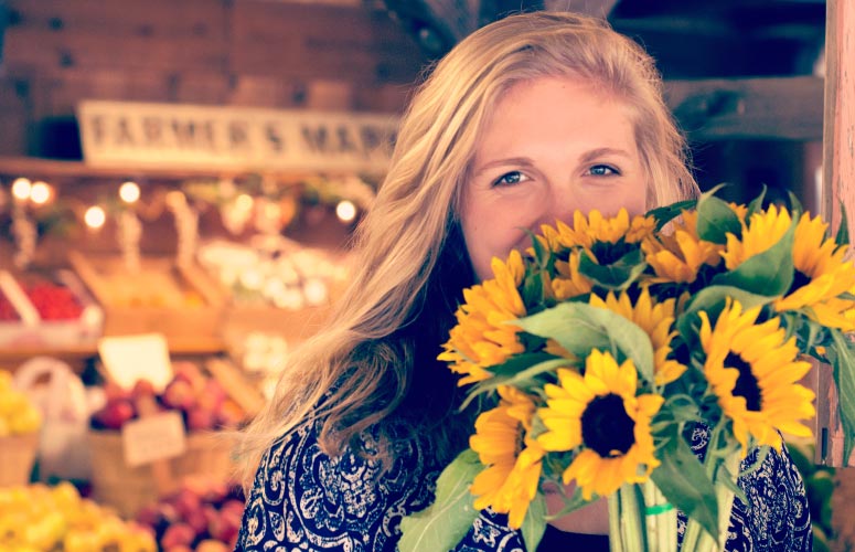 Blonde young woman hides her yellow teeth with a bouquet of yellow sunflowers at a farmers market