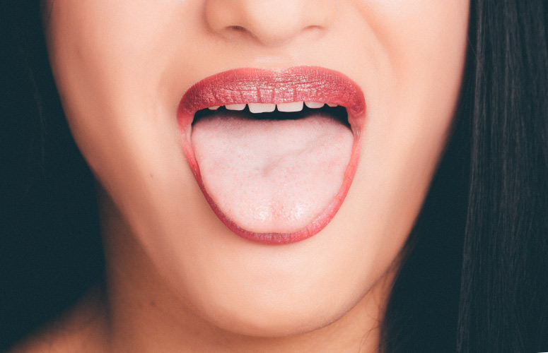 Closeup of a woman with magenta lips sticking out her pink tongue