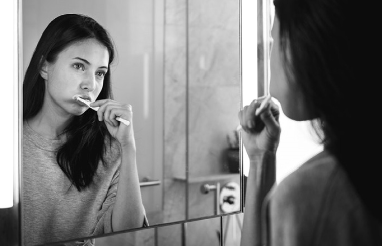girl looking in the mirror brushing her teeth to prevent cavities