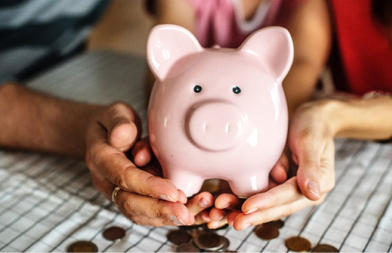 hands holding a pink piggybank spilling coins out the bottom