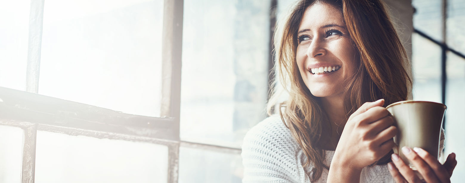 Woman looking out window smiling holding cup of coffee