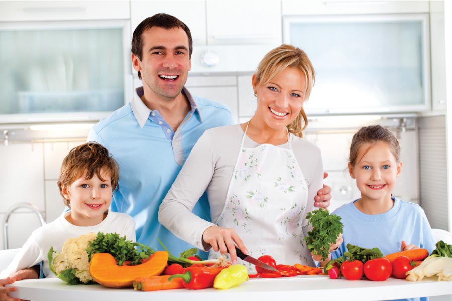 Family of four in the kitchen with a counter full of healthy fruits and vegetables.