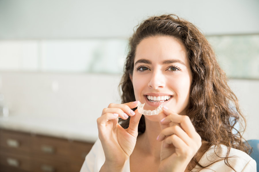 Smiling woman holding an Invisalign clear aligner.
