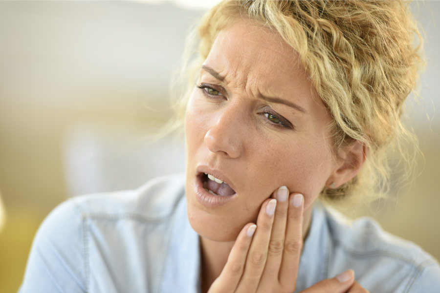 Blond woman with her hand to her cheek indicating tooth pain.