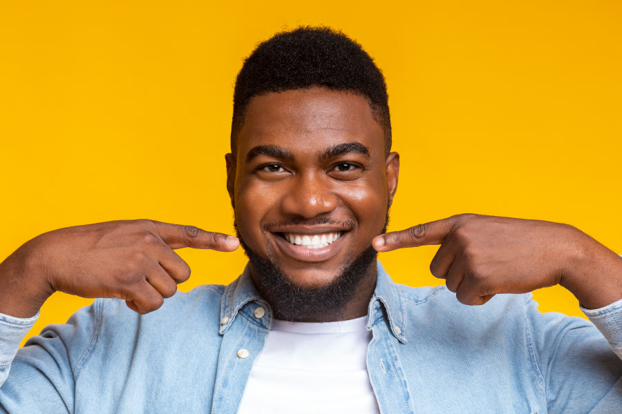 Smiling man in front of a yellow background pointing to his white smile.