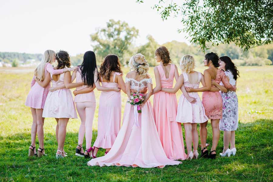 A back view of a line of attendants and a bride in a green meadow.