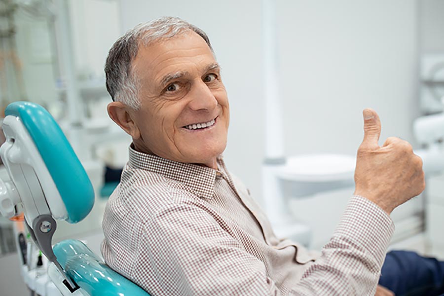 Gray haired senior man smiling and giving the thumbs up sign from the dental chair.