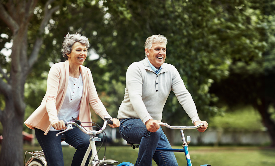 two older adults smiling while riding bicycles