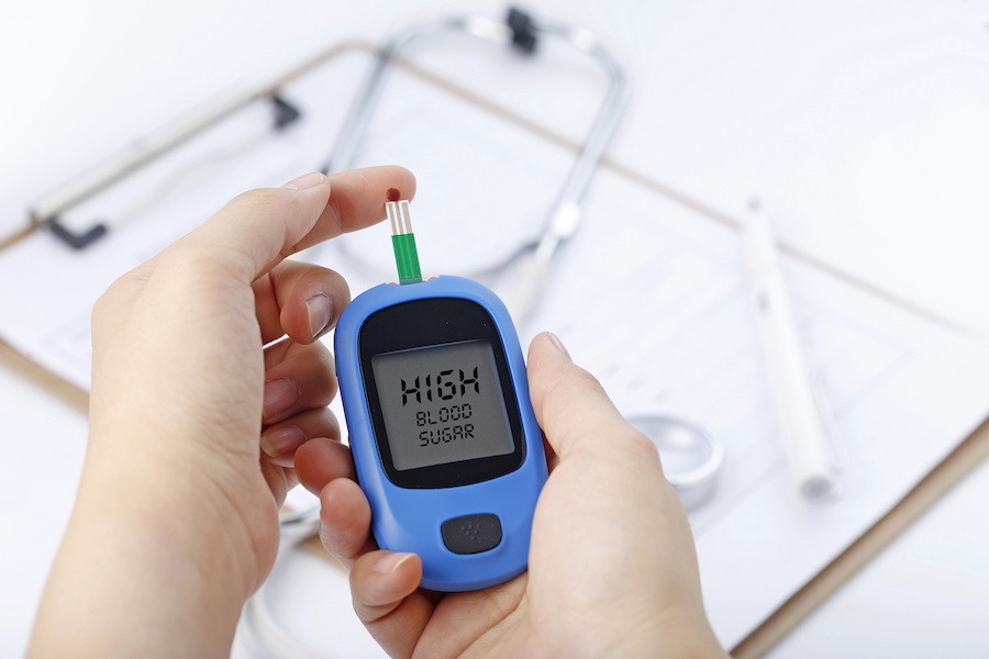 Photograph of a hand holding a blood glucose monitor for diabetes, showing high blood glucose. Oral health and diabetes.